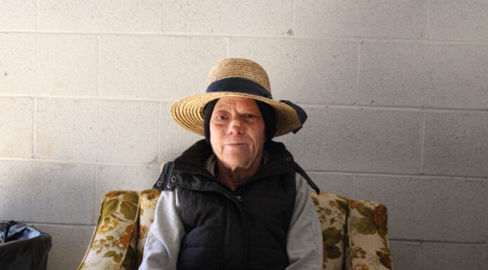 Athens homeless camp offers access to permanent housing for residents in temporary camp site White woman in in straw hat wearing a bandage across her nose sits on a floral chair in front of white background.