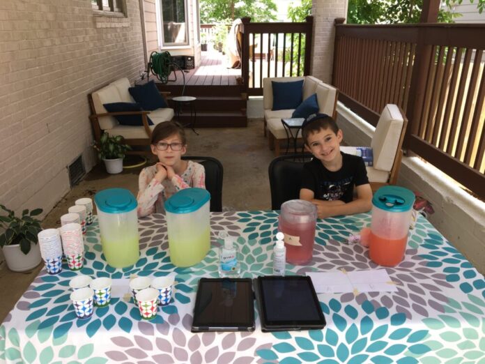 Two children sit at lemonade stand smiling