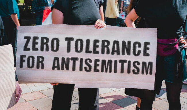 ‘We will be back’: Backer of antisemitic hate crimes bill vows to try again White sign with black lettering being held by man in a crowd