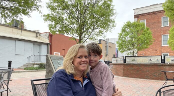 Georgia aims to boost childhood literacy with new law signed by Gov. Kemp White woman with blonde hair sits in chair hugging young boy with brown hair outside in front of trees and brick building