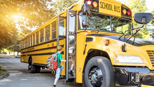 child wearing green shirt and red backpack boards a yellow school bus