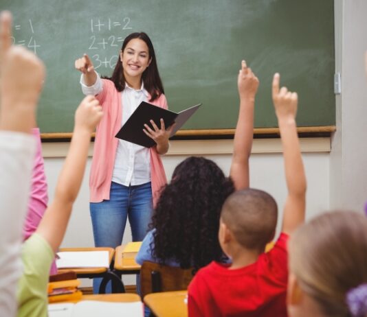 Georgia passes another raise for teachers – is it enough to alleviate the shortage? White teacher stands in front of chalkboard with students raising hands