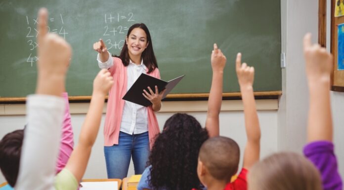 Georgia passes another raise for teachers – is it enough to alleviate the shortage? White teacher stands in front of chalkboard with students raising hands