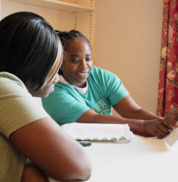 Atlanta participants reflect on first year in guaranteed income program Black woman in green t-shirt presenting the Georgia Resilience and Opportunity Fund paper to Black woman in tan t-shirt