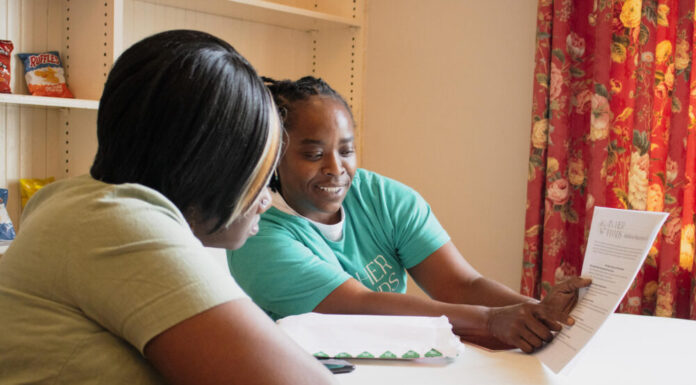 Atlanta participants reflect on first year in guaranteed income program Black woman in green t-shirt presenting the Georgia Resilience and Opportunity Fund paper to Black woman in tan t-shirt