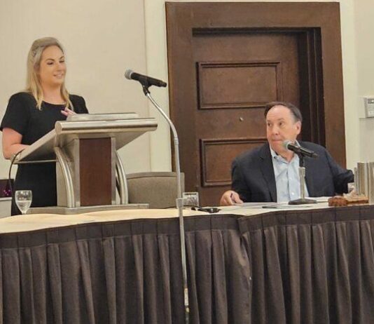 Georgia aims to boost low literacy rate, in part by copying Mississippi’s successful blueprint White woman wearing a black dress to the left standing at a podium speaking to her right is a white man sitting down wearing suit
