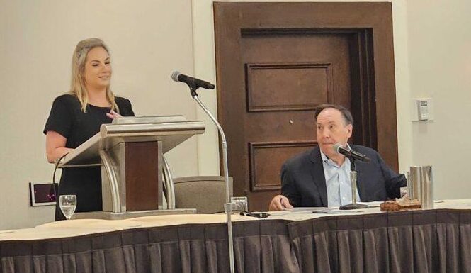 Georgia aims to boost low literacy rate, in part by copying Mississippi’s successful blueprint White woman wearing a black dress to the left standing at a podium speaking to her right is a white man sitting down wearing suit