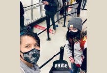 Post COVID-19 education in isolation Left to right white mother takes selfie with mask on in airport security line with son and daughter who are both wearing hats and masks
