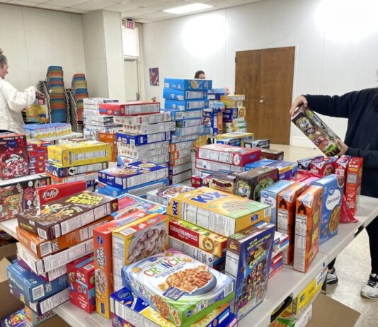 Cobb nonprofit meal drive kicks off holiday season Three volunteers stand around a table piled with dozens of boxed food items.