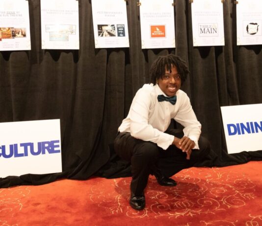 Atlanta homeless youth program helps students attend college Atlanta student homelessness: Young Black man with black dreads in formal wear with black bow tie crouches on orange carpet in front of black curtain with several hanging paper signs.