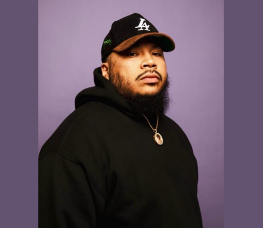 Everyday Hero: Kali Cunningham’s non-profit gives back to the community Headshot of Kali Cunningham, a young adult male with Los Angeles Dodgers hat and black beard wearing black hooded sweatshirt and a gold chain against a plain purple background.