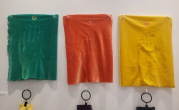 Visitors break all the rules at hands-on art exhibit Three pieces of velvet embroidered with hands are displayed on a white wall. From left to right, the pieces are green, red, and yellow.