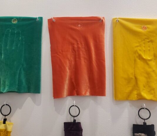 Visitors break all the rules at hands-on art exhibit Three pieces of velvet embroidered with hands are displayed on a white wall. From left to right, the pieces are green, red, and yellow.