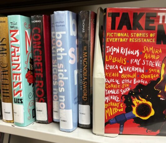 Georgia Senate targets American Library Association in new legislative push A row of multicolored books are lined up on a plain shelf. All have their spines facing the camera. On the right, the book "Take the Mic: Fictional Stories of Everyday Resistance" is turned so the cover faces the camera. The cover is red, the title is in black and white, and it features an illustration of a side profile of a Black woman yelling into a microphone that is on fire. There are 11 authors whose names are scattered across the cover.