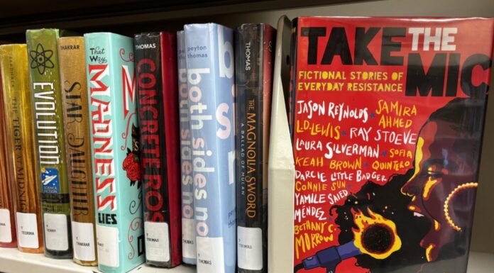 Georgia Senate targets American Library Association in new legislative push A row of multicolored books are lined up on a plain shelf. All have their spines facing the camera. On the right, the book "Take the Mic: Fictional Stories of Everyday Resistance" is turned so the cover faces the camera. The cover is red, the title is in black and white, and it features an illustration of a side profile of a Black woman yelling into a microphone that is on fire. There are 11 authors whose names are scattered across the cover.