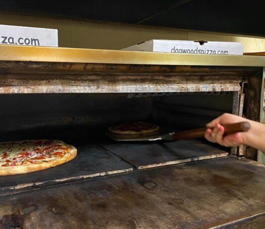 Creating a legacy: Dagwood’s Pizza and Deli’s 42-year journey A hand holding a pizza peel scoops a pizza out of a large oven. A second pepperoni pizza bakes in the oven to the left of the first one.