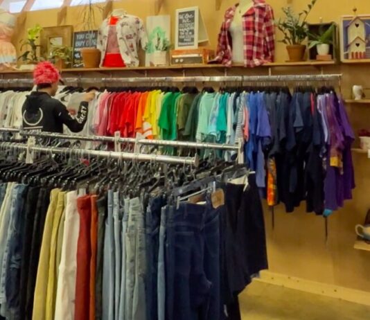 Affordable fashion resale encourages sustainability Wide shot of racks of colorful clothing in a secondhand store. Two men are sorting through the racks of clothes.