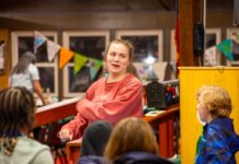 From camper to staff: How one camp’s mission changes lives A woman with tied-back brown hair wearing a red sweatshirt dances with a group of children. The kids are dressed in casual clothing.