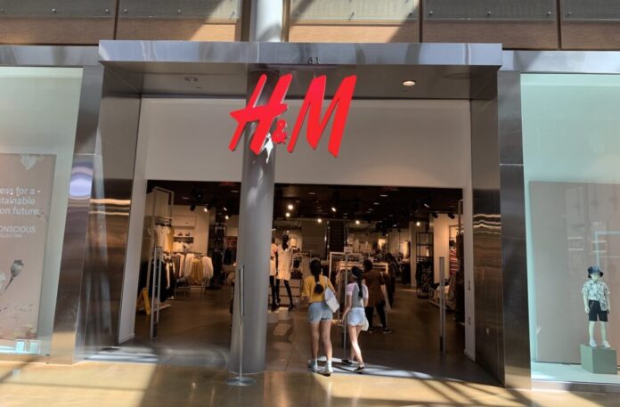 A wide shot of the front of H&M. The letters are a neon red sign and the store has large glass windows.
