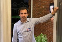 Georgia House candidate offers inside look at campaign process A man knocking on an open door with a blue shirt. He is smiling and is wearing a campaign tag. The background is a brick house and a dark sky.