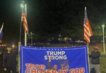 Trump holds rally in Duluth to encourage voting Two Japanese men wearing all black hold American flags and a large blue sign with a photo of Donald Trump after he was shot. The text reads, "Trump strong, Chosen by God."