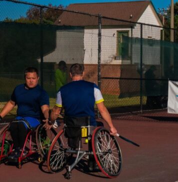 Heart and skill on display at USTA Wheelchair Tennis Championship Two men in wheelchairs dressed in athletic-wear holding tennis rackets high-five each other on a tennis court. There is a banner behind them that reads, "USTA, find yourself in the game, Southern."