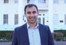 Georgia elects first democratic socialist to state House of Representatives A man with short, dark hair wearing a light blue button-up and navy blue blazer stands in front of a house and smiles at the camera.