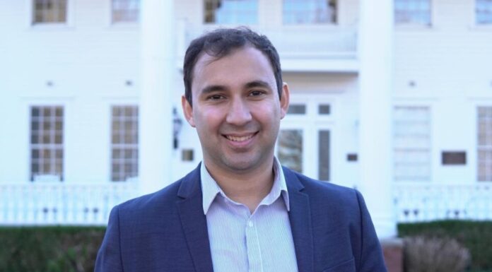 Georgia elects first democratic socialist to state House of Representatives A man with short, dark hair wearing a light blue button-up and navy blue blazer stands in front of a house and smiles at the camera.