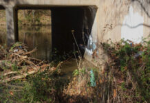 How west Atlanta’s residents fight environmental racism, injustice A concrete bridge sits above a creek with a dam full of sticks and plastic garbage. Bushes along the creekside are also full of discarded water bottles and plastic bags.
