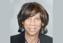 Everyday Hero: Polio survivor’s journey of service and resilience A portrait of a Black woman wearing a black blazer, a blue and green necklace with matching earrings, and straight dark brown hair with highlights cut to her shoulders.