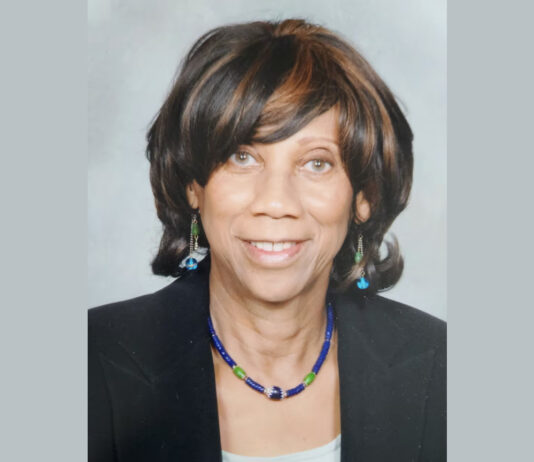 Everyday Hero: Polio survivor’s journey of service and resilience A portrait of a Black woman wearing a black blazer, a blue and green necklace with matching earrings, and straight dark brown hair with highlights cut to her shoulders.
