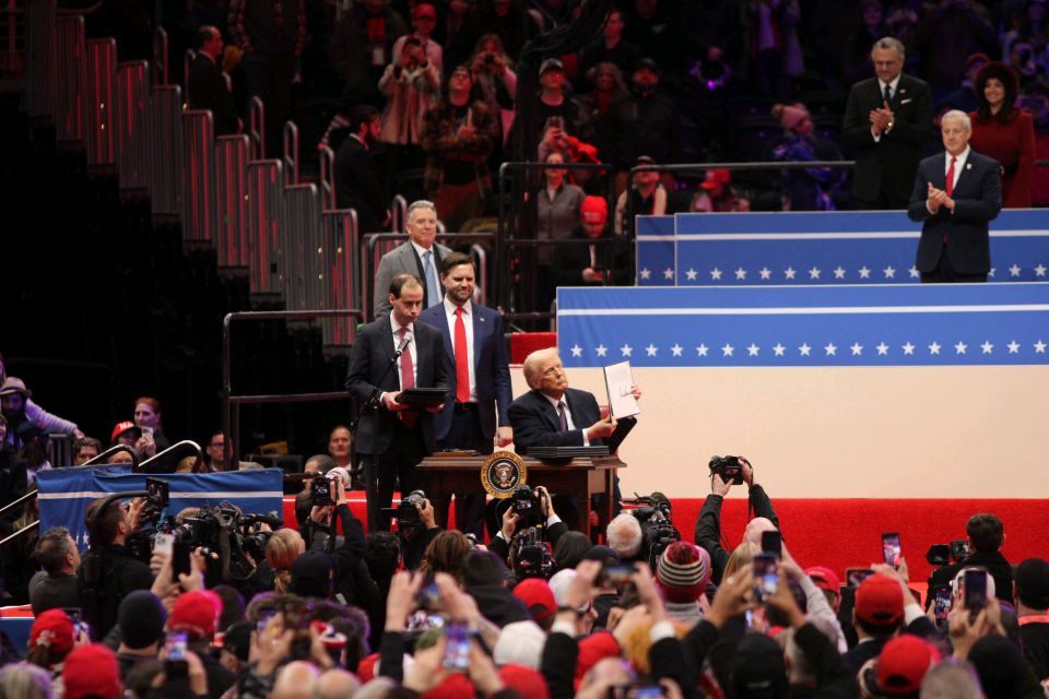 President Donald Trump signs a series of executive orders in front of a large crowd of supporters.