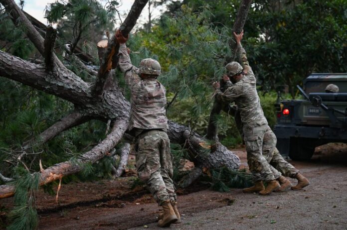 Three Georgia Army National Guards clear a downed tree from the road.