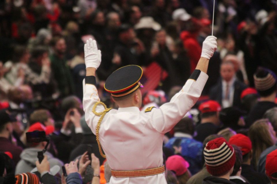 Band conductor leads the band wearing a white uniform.