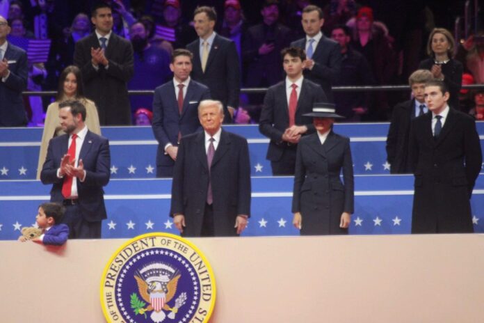 President Donald Trump stands and watches Inaugural Parade with first lady (left) and Vice President JD Vance (right).