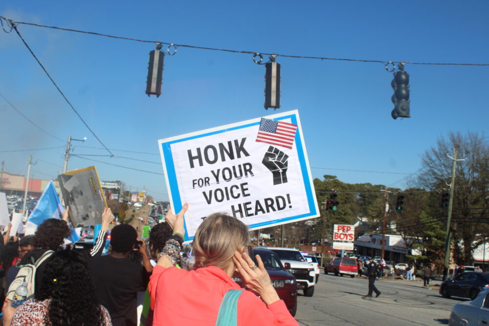 Protester holding a sign "Honk for your voice heard" (Zaire Breedlove/ Fresh Take Georgia).